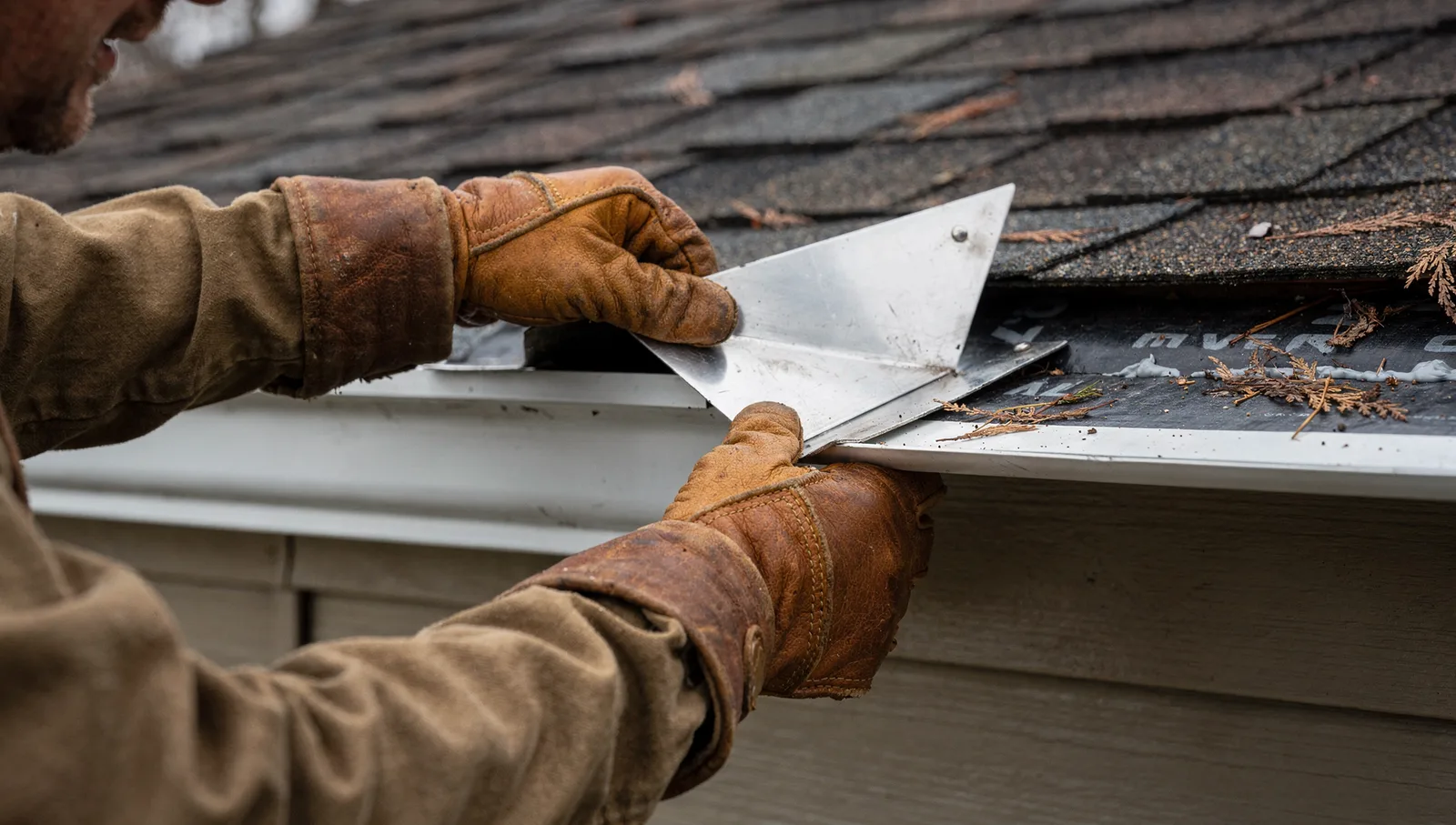 Roofer installing an aluminum kick-out flashing diverter where a sloped roof meets siding above a gutter.